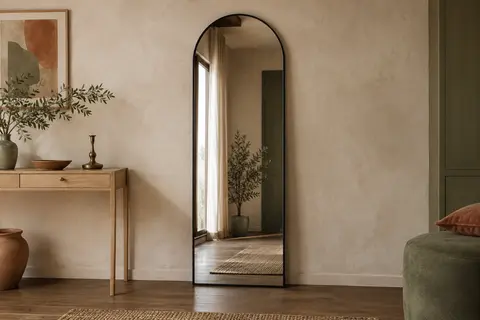 Miroir en arche à cadre noir posé contre un mur crème dans un intérieur lumineux et chaleureux
