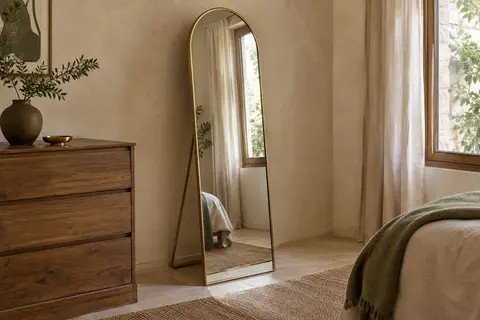 Miroir en arche pleine hauteur avec cadre doré et support pliable dans une chambre lumineuse